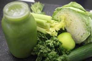 Home Vers geperste green juice voor het sporten in een glas met groene ingrediënten op de achtergrond